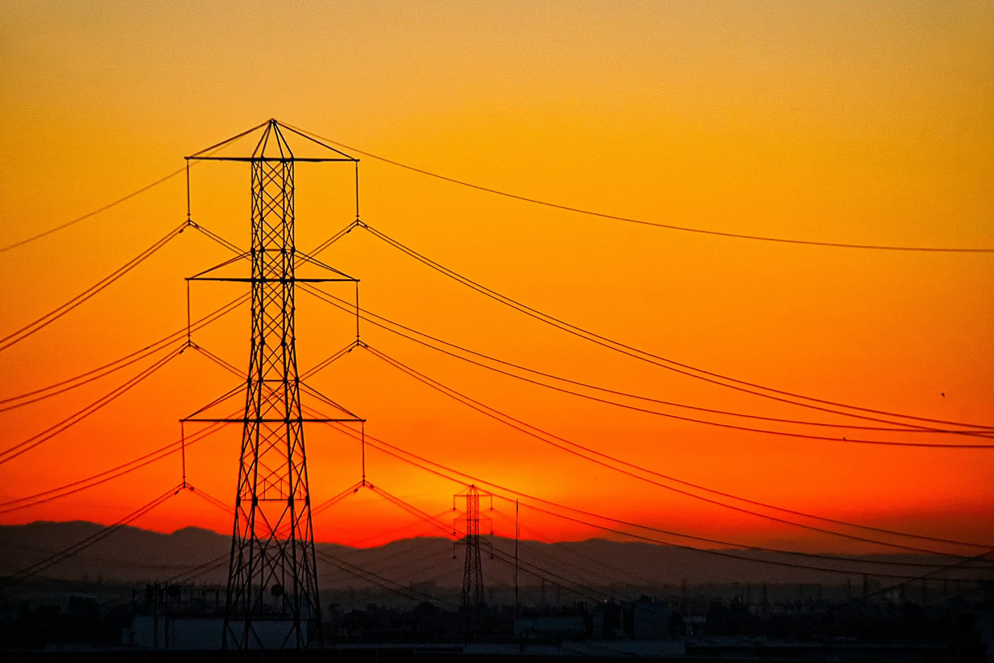 a transmission tower in front of an orange California sunset